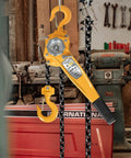 0.75 Ton Manual Lever Chain Hoist with G80 galvanized carbon steel construction, yellow handle, hanging in a workshop.