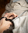 Hands using 10 Inch Bent Handle Industrial Shears for Heavy Duty Cutting of Upholstery, Carpet, and Drapery Materials on fabric.