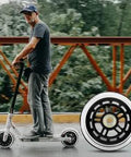 Person riding a scooter with a close-up of 100mm scooter replacement wheels pair with ball bearings black pro stunt wheels.