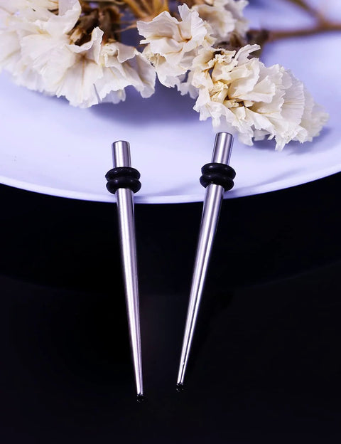 10G Ear Gauges Stretching Kit With 316L Surgical Steel Tapers And Insertion Pins Includes 2 Pieces For Ear Lobe Septum Tongue And Nipple Piercing Smooth Polished Body Jewelry Tools For Safe Easy Stretching At Home, two steel tapers with rubber stoppers on a plate with flowers