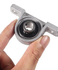 Hand holding Six Pack KP000 10mm Pillow Block Bearing Self Aligning Mounted Flange Zinc Alloy Base for machinery.