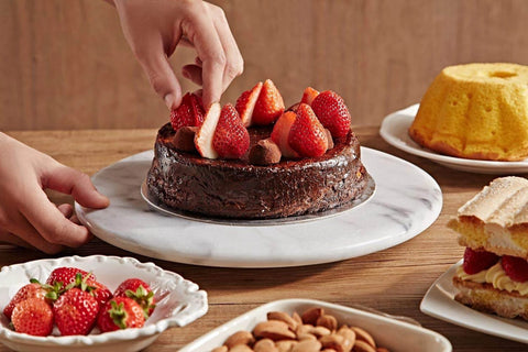 Person placing strawberries on a chocolate cake on a 12 inch white marble lazy susan turntable with aluminum bearing.