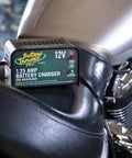 Close-up of 12V 1.25 Amp Car and Motorcycle Battery Charger and Maintainer on a motorcycle seat, showing adaptive smart charging