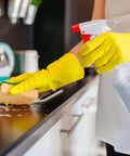 Person cleaning counter with 16oz Adjustable No Leak No Clog Spray Bottles 2 Pack BPA Free HDPE For Cleaning Solutions Plants, wearing yellow gloves.