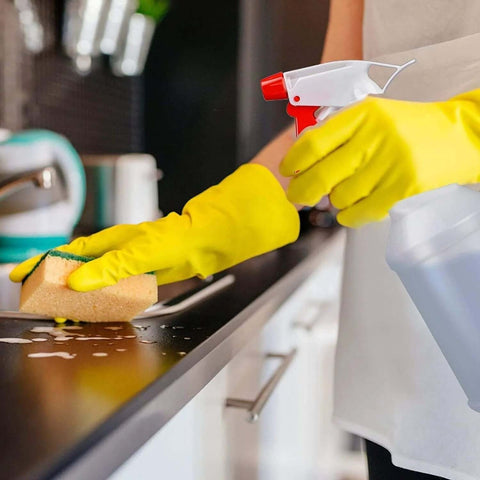Person cleaning counter with 16oz Adjustable No Leak No Clog Spray Bottles 2 Pack BPA Free HDPE For Cleaning Solutions Plants, wearing yellow gloves.