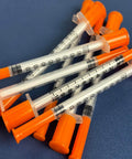 1cc Syringes With 31G Needle 5/16 Inch 8mm Individually Packaged 36 For Lab Use And Calibration, orange capped, scattered on blue surface