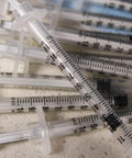 Pile of 1 mL Syringes With 31G Needle Five Sixteenth Inch Length Individually Wrapped Pack Of 100 For Lab Use scattered on a surface.