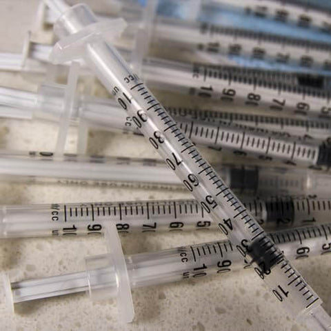 Pile of 1 mL Syringes With 31G Needle Five Sixteenth Inch Length Individually Wrapped Pack Of 100 For Lab Use scattered on a surface.