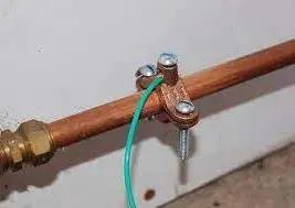 Heavy Duty Bronze Water Pipe Ground Clamp Fits One Quarter To Two Inches securing a water pipe with green grounding wire attached.