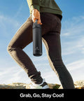 Person holding a black 26 oz insulated stainless steel water bottle with a 2-in-1 straw and spout lid, perfect for outdoor activities.