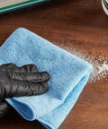 Blue 12x12 inch microfiber general purpose cloth; 12-pack, shown with a gloved hand on a wood surface.