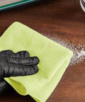 Close-up of Sam 12x12-inch yellow microfiber general-purpose cloth (12-pack) held by a gloved hand on a wood surface