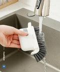 Person rinsing 3-In-1 Removable Window Slot Brush With Hidden Scraper under faucet, showcasing cleaning tool use in kitchen sink.