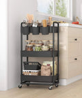 3 Tier Rolling Storage Cart With Lockable Wheels And Extra Hanging Cups For Kitchen, Bathroom, Living Room Or Office Black Heavy Duty Iron Frame, Sturdy Plastic Trays, Smooth Rolling, Easy Assembly By JIUYOTREE in kitchen corner filled with supplies.