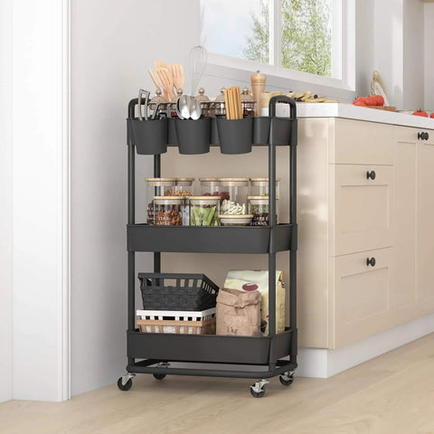 3 Tier Rolling Storage Cart With Lockable Wheels And Extra Hanging Cups For Kitchen, Bathroom, Living Room Or Office Black Heavy Duty Iron Frame, Sturdy Plastic Trays, Smooth Rolling, Easy Assembly By JIUYOTREE in kitchen corner filled with supplies.