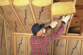 Worker installing Premium R30 Fiberglass Batt Insulation 16 By 48 Inch Kraft Faced Vapor Barrier Covers in ceiling.
