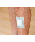 Nexcare bandage tape on leg; white adhesive pad with clear surrounding tape, gentle for sensitive skin.