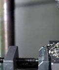 Close-up of a drill bit clamped in a metal vise with metal chips around the work area