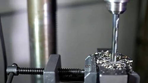 Close-up of a drill bit clamped in a metal vise with metal chips around the work area