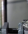 Drill bit close-up in a drill press cutting metal, secured in a vise with metal shavings.