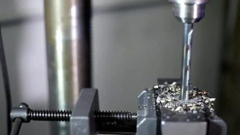 Drill bit close-up in a drill press cutting metal, secured in a vise with metal shavings.