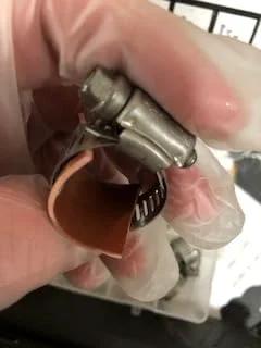 Gloved hand holding a patch and clamp from Emergency Pipe Repair Kit With 12 Patches And Clamps For Quick Leak Fix On One Quarter To One And A Quarter