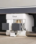 Cricut knife blade and drive housing installed under Cricut Maker; white unit with gray grips and gold screws.