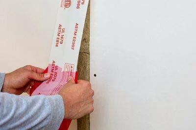 Applying Fire and Water Barrier Tape FWBT4 4 in x 75 ft to a construction joint for smoke and sound isolation.