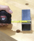 Hand measuring metal rectangular tube with tape measure on wooden workbench