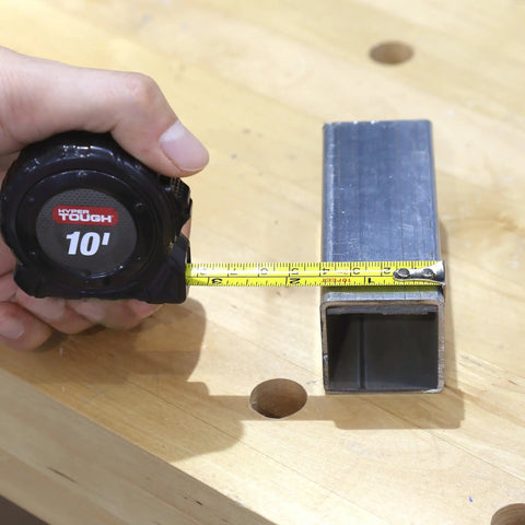 Hand measuring metal rectangular tube with tape measure on wooden workbench