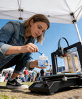 Person applying 3D Printer Lube Kit 100g Bearing Oil With Brush Gear Grease to 3D printer at outdoor workshop event