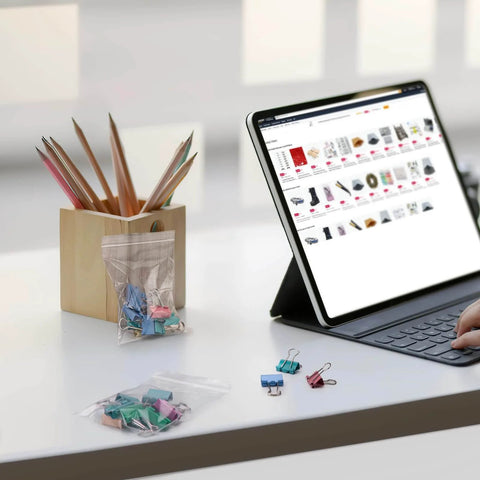 Tablet next to 400 Pcs Clear 3x4 Inch Jewelry Bags 2 Mil Resealable Zip Bags and binder clips on a desk.
