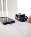Person charging phone using Power Core 12 Brushless 12V Compact Drill Driver and Impact Driver Kit with 2.0Ah Battery and PWR Jump Charger