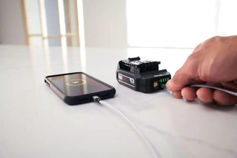 Person charging phone using Power Core 12 Brushless 12V Compact Drill Driver and Impact Driver Kit with 2.0Ah Battery and PWR Jump Charger