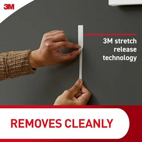 Person demonstrating removal of Heavyweight Picture Hanging Strips XL 20 Lb 16 Pairs 32 Strips with 3M stretch release technology.