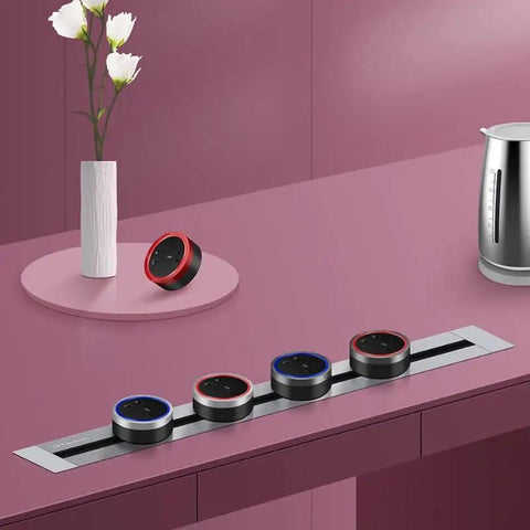 Sleek Concealed Power Track Socket Offering Four Dedicated Plug Outlets For Lowkey Kitchen Counter Organization And Modern Home Electrical Flexing Heavy Duty Sandblasted Aluminum Finish with red and blue outlets on pink countertop.