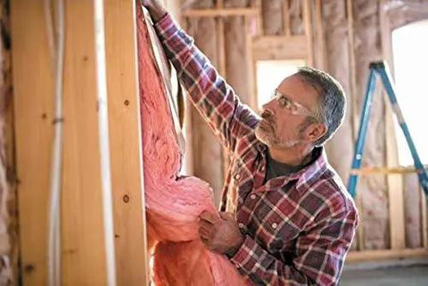 Man installing Two Pack R13 Pink Kraft Faced Fiberglass Insulation Rolls For 2x4 Wall Cavities 15 Inches By 32 Feet in wall.