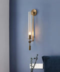 Modern Long Tube Wall Sconce In Brushed Gold Metal And Frosted Glass casting a warm glow on blue wall beside a bedside with decor.