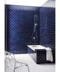 Modern bathroom with navy blue tiled walls and a white bathtub, featuring a handheld showerhead and towel.