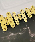 Close-up of the Five Pcs Brushed Brass Deco Furniture Hinges Set shown on a table, designed for jewelry boxes, cabinets, and more.