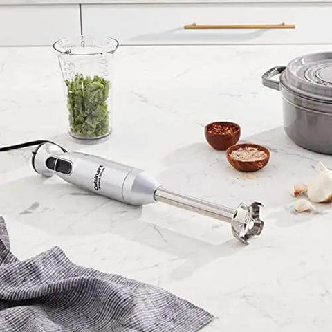 Heavy Duty Corded Stick Blender With Two Speed Toggle Makes Silky Smoothies And Creamy Broths In A Jiffy With Whisper Quiet Motor In Sleek Silver on kitchen countertop with herbs.