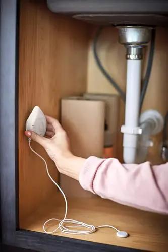 Hand installing Flo Smart Water Leak Detector 3 Pack under sink for real time alerts and round the clock leak monitoring.