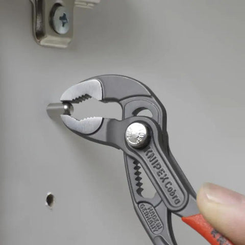Cobra Water Pump Pliers, 5 Inch, Red, Adjustable Pliers With Self-Locking Teeth in use on pipe with pinch guard feature visible
