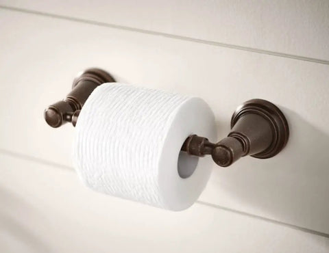 Wall-mounted toilet paper holder with bronze finish and white roll, suitable for bathrooms, classic design, secured on a wall.