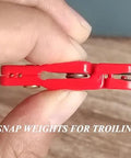 Close-up of a red plastic snap weight release clip for trolling planer-board fishing, held between fingers.
