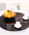 39 Inch Glass Lazy Susan Turntable With Six Super Slick Wheels Hella Sturdy Rotating Serving Tray featuring fruits and coffee cups on a black glass surface.