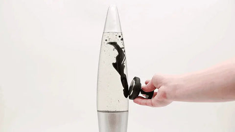 Decorative Retro Rocket Ship Ferrofluid Lava Lamp with Magnetic Black Wax in Clear Liquid, silver base, hand holding magnet influence.