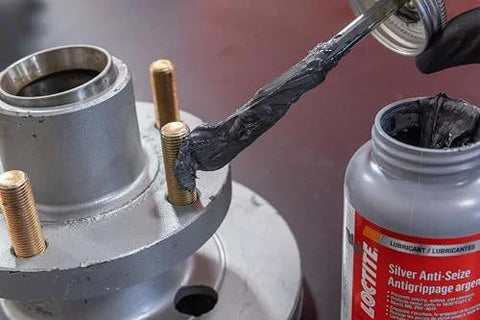 Loctite Automotive Silver Anti-Seize lubricant bottle applying to bolt threads on a wheel hub assembly.