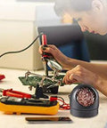 Person using Pro DIY Soldering Iron Kit Four In One With Brass Tip Cleaner That Works Without Water Point Six Millimeter Solder Wire Fifty Gram Rosin Flux Paste Ten Gram No Clean Core Solder Handy Welding Tool Set For Home Projects on electronics at a workbench.