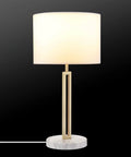 Paloma Table Lamp By Novogratz X Globe with modern glam cutout metal body, matte brass finish, white faux marble base, white fabric shade.